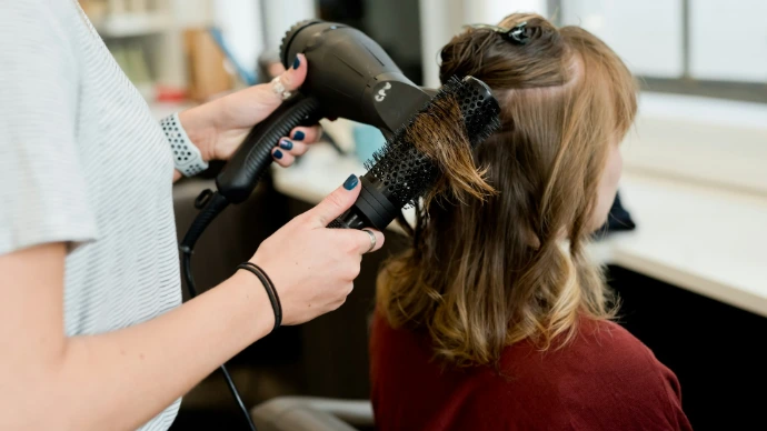 A hairstylist using a blow dryer and round brush on a client's hair